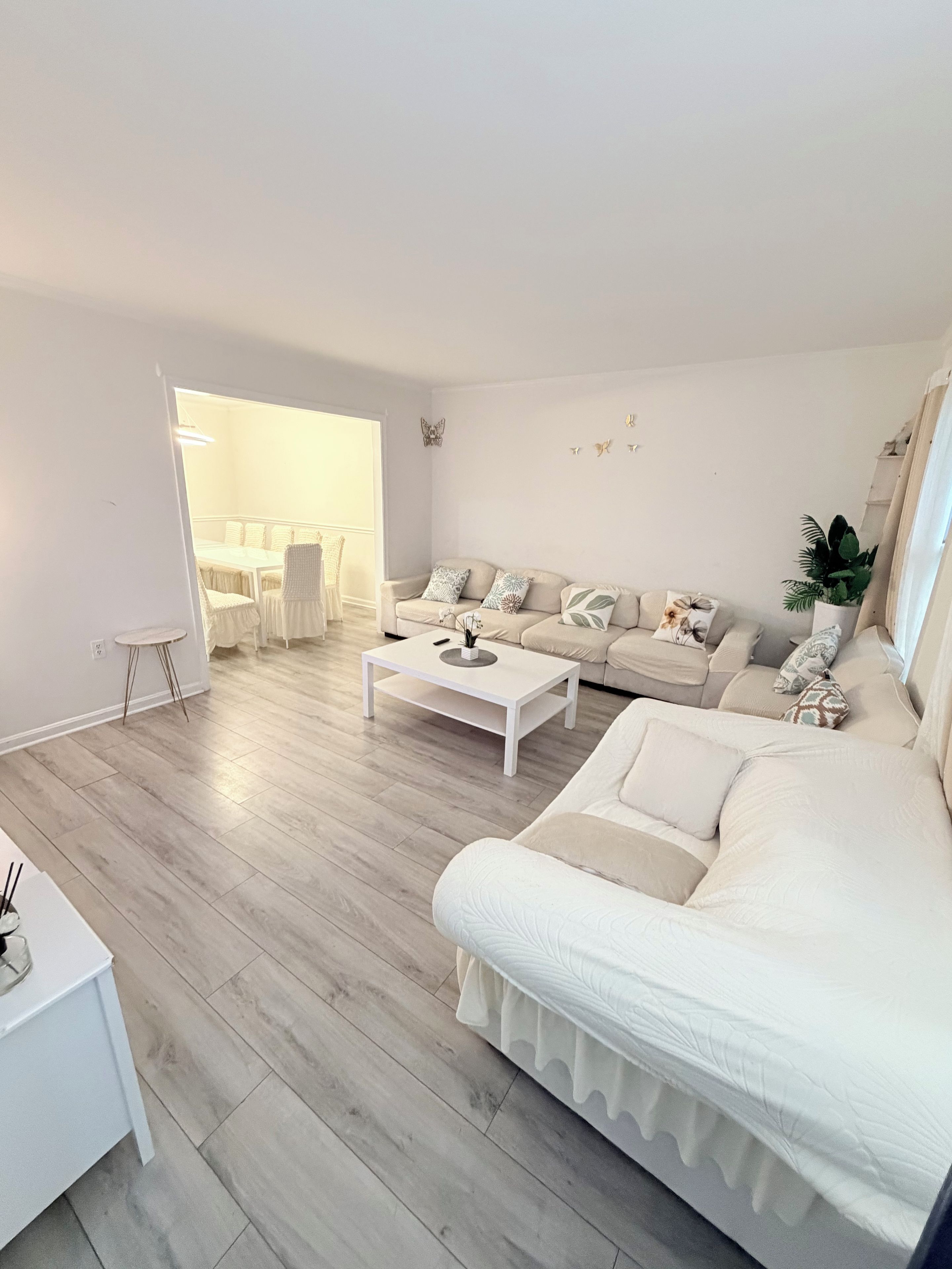 A modern living room with a white sofa, a coffee table, and a dining area with a white table and chairs.