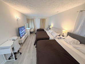 A hotel room with two beds, a desk, a chair, a TV, and a lamp.