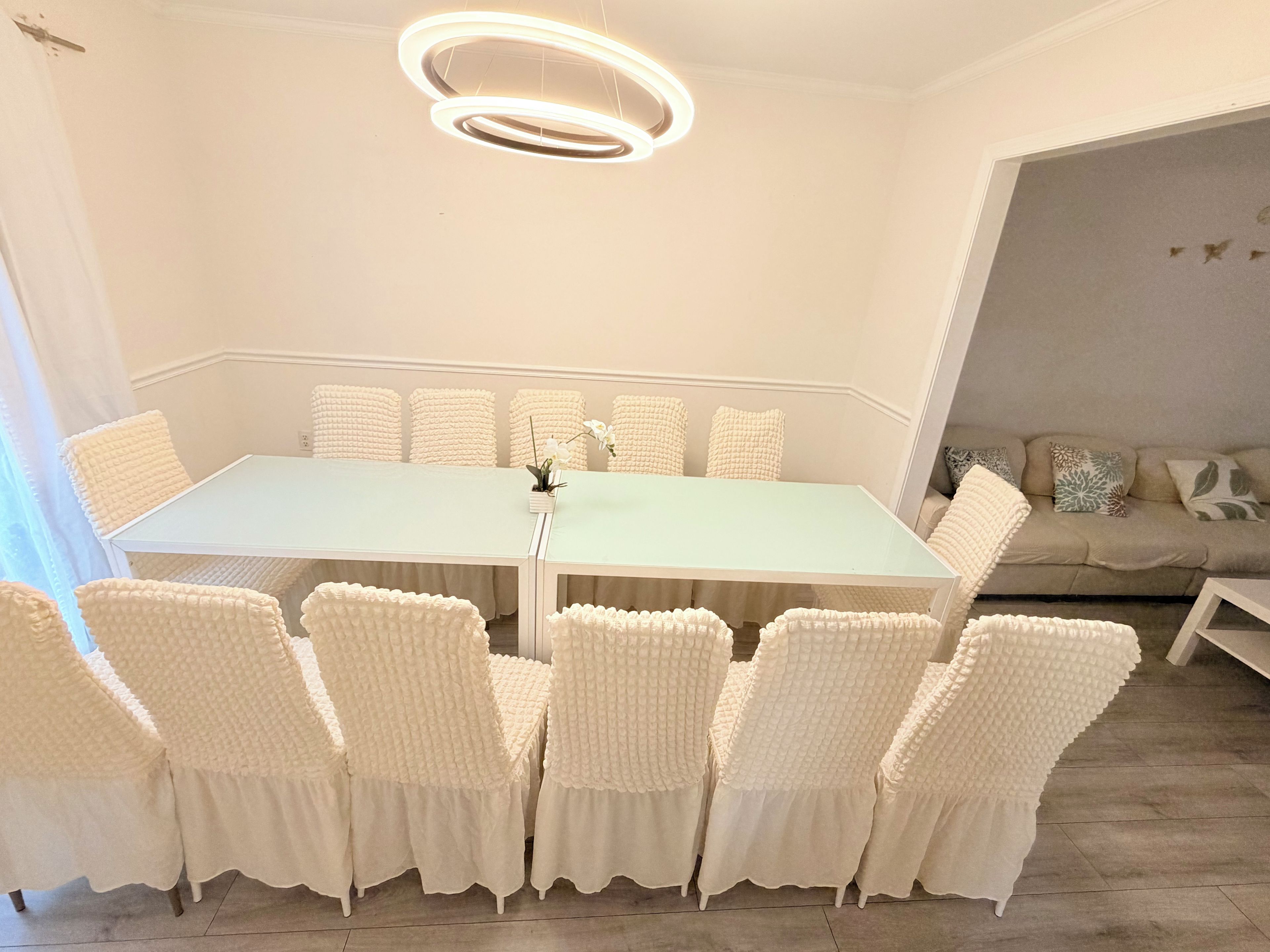 A dining area with a light green table, white cushioned chairs, and a modern circular ceiling light.
