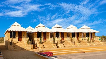 A row of traditional desert-style tents with a flat roof, arranged in a line with a paved walkway in front.