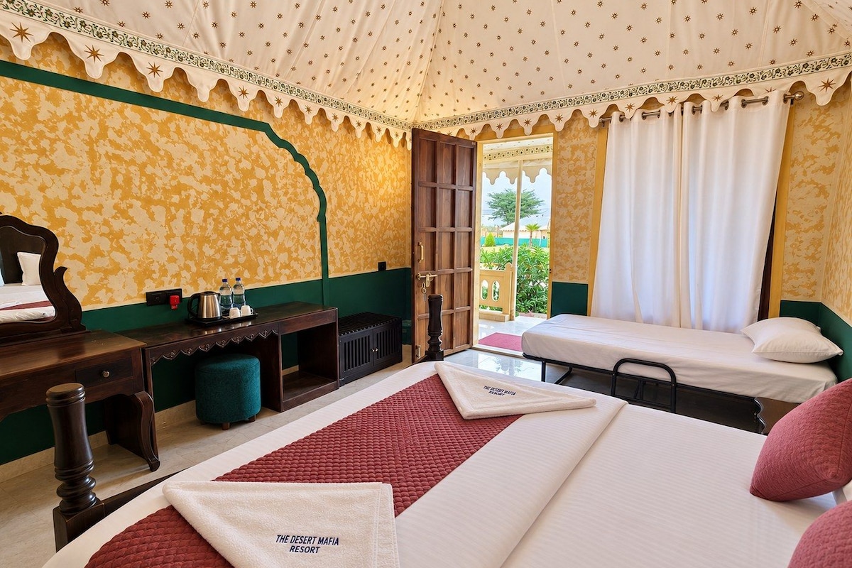 A hotel room with a bed, a desk, a chair, a small table, and a window with curtains.