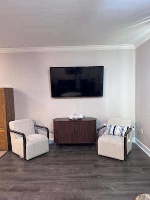 A living room with a flat-screen TV mounted on the wall, two armchairs, a round wooden side table, and a dark wooden floor. - Escape to Cloud 904 @ Tidewater Beach Resort on the water! (Panama City Beach)