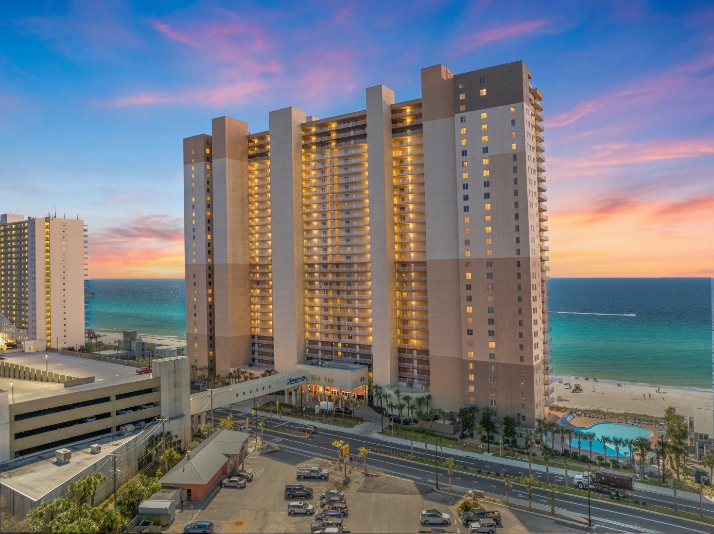 A high-rise hotel with multiple balconies, a parking garage, and a pool area.