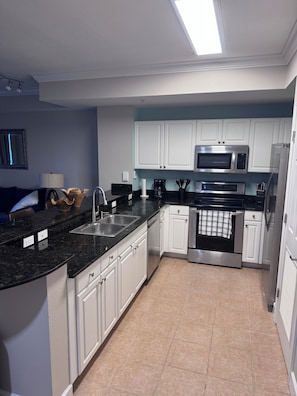 A modern kitchen with white cabinets, a stainless steel microwave, and a black countertop. - Escape to Cloud 904 @ Tidewater Beach Resort on the water! (Panama City Beach)