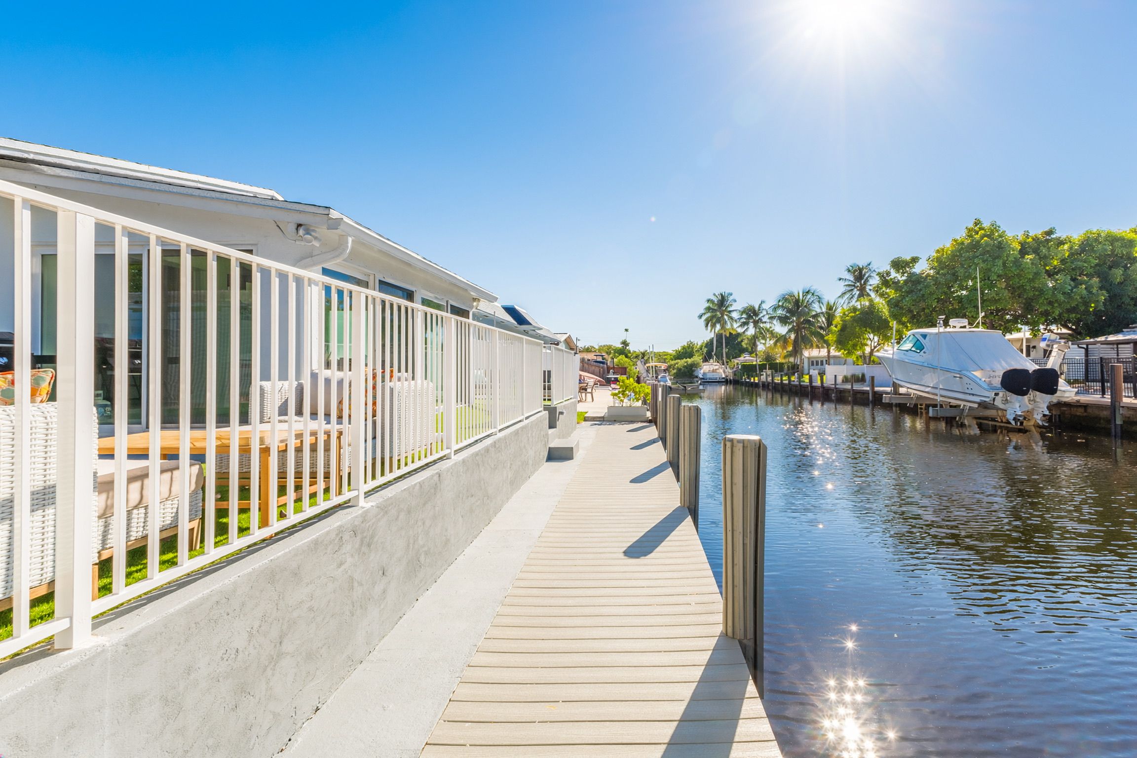 A waterfront property with a wooden deck, a white fence, and a marina with boats.
