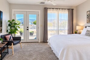 Ein Hotelzimmer mit Bett, Schreibtisch, Stuhl, Pflanze und Blick ins Freie.