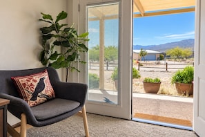 A room with a grey armchair, a large potted plant, and a view of a desert landscape through a glass door. - Clarkdale Suite Mingus Mountain Verde Valley Views (Clarkdale)