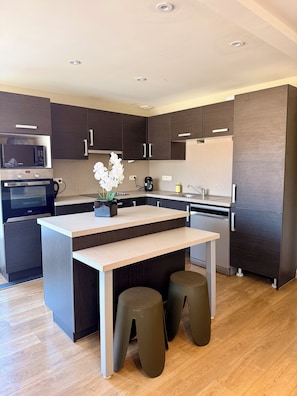 A modern kitchen with dark cabinetry, a central island, stools, and built-in appliances. - Vrbo Property (Vesoul)