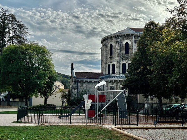 A historic stone building with arched windows and a bell tower, surrounded by a fenced playground area with a slide and climbing structure. - Vrbo Property (Vesoul)