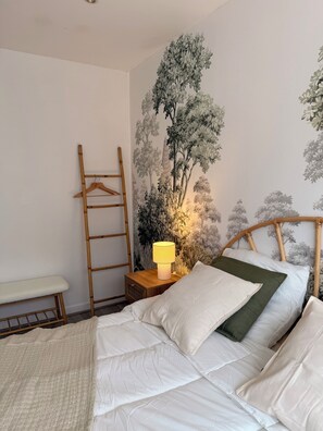 A bedroom with a bed, a bedside table with a lamp, a wooden ladder, and a wall with a floral mural. - Vrbo Property (Vesoul)