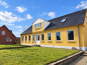 Ein gelbes Gebäude mit flachem Dach und vielen Fenstern, umgeben von einem gepflegten Rasen.