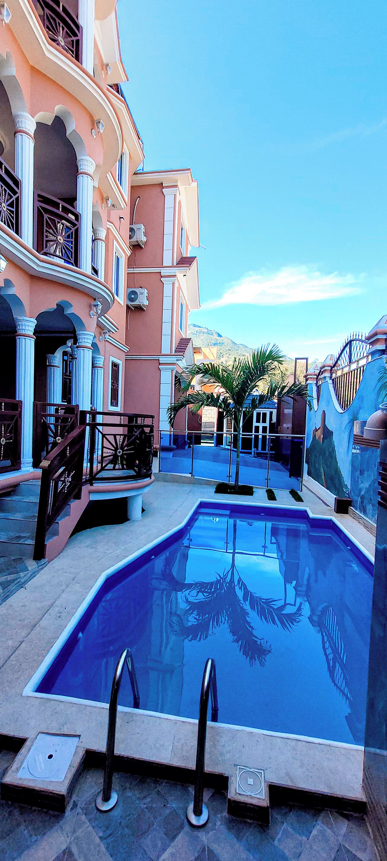 A swimming pool with a clear blue water surface, surrounded by a building with balconies and a decorative wall.