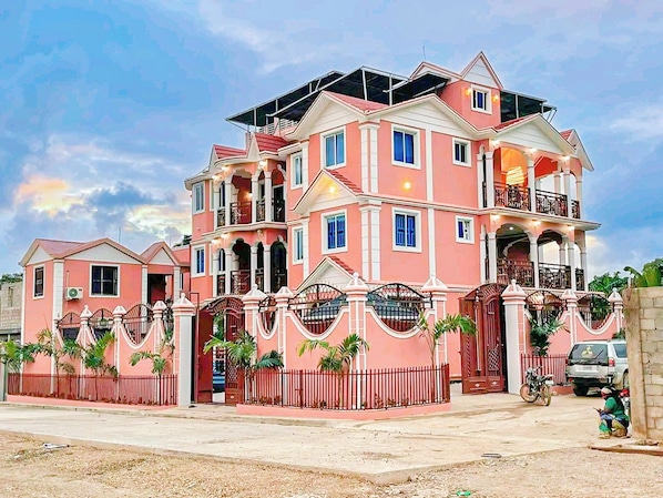 A multi-story pink house with a gated entrance, a balcony, and a motorcycle parked in front.