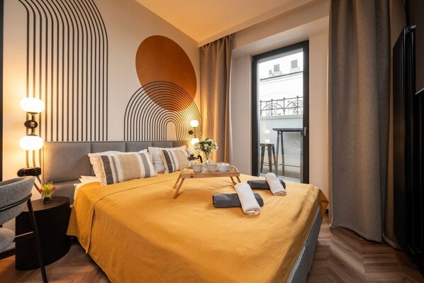 A hotel room with a bed, bedside table, lamp, and a view of the outside. - Łódź Roosevelta Studio C — Balcony & A/C (Łódź)
