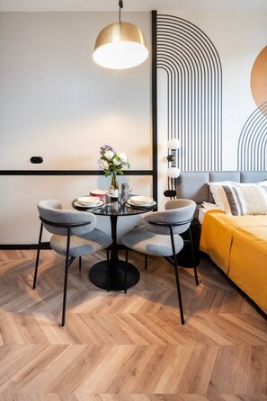 A modern dining area with a round table, four chairs, and a pendant light. - Łódź Roosevelta Studio C — Balcony & A/C (Łódź)