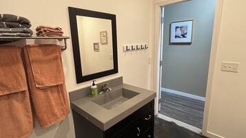 A bathroom with a sink, mirror, towel rack, and a door leading to another room.