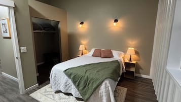 Un dormitorio con una cama, dos lámparas de noche, una manta verde y una mesita de noche.