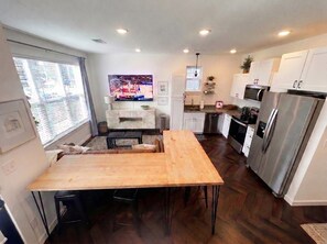 A modern kitchen with a wooden dining table, stainless steel appliances, and a large window with blinds. - The Fayetteville Trail House-1.5 miles from the U of A & next to Centennial Park (Fayetteville)