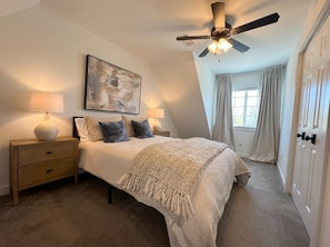 A bedroom with a bed, two bedside tables, a ceiling fan, a window with curtains, and a door. - The Fayetteville Trail House-1.5 miles from the U of A & next to Centennial Park (Fayetteville)