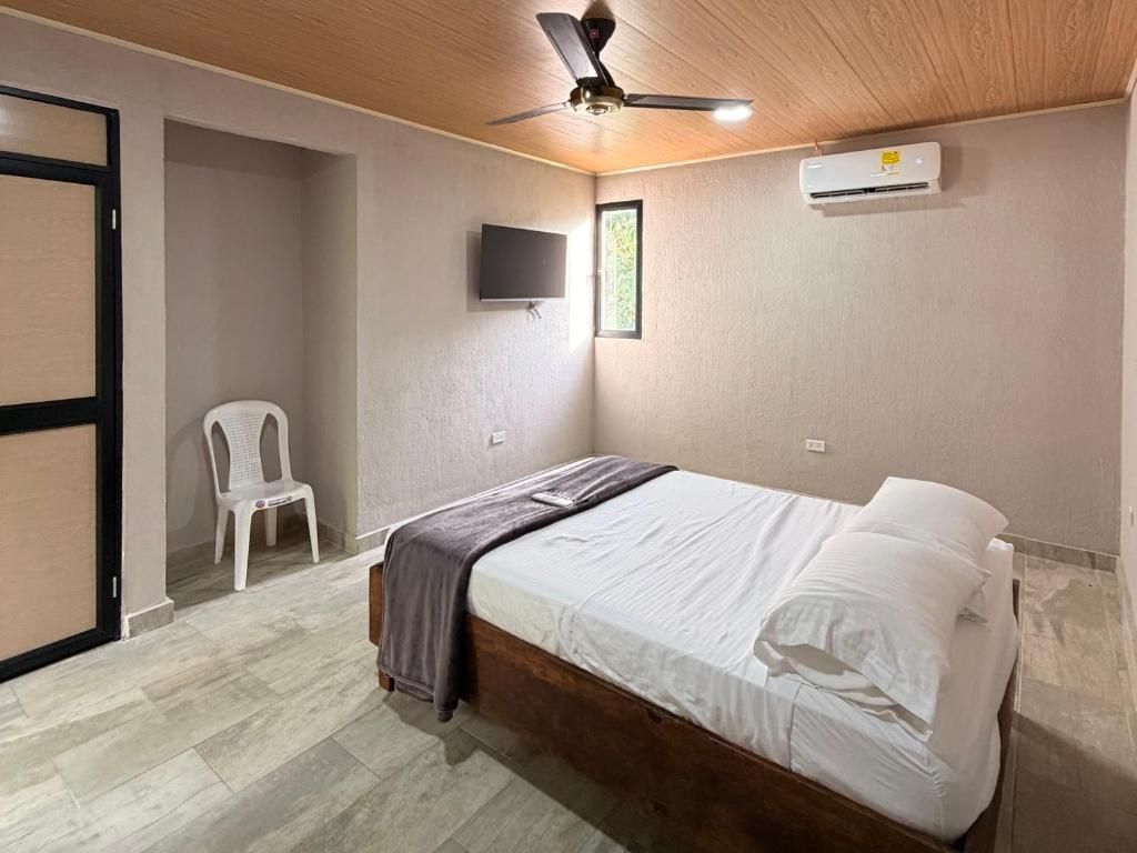 Un dormitorio con cama, ventilador de techo, televisor montado en la pared y aire acondicionado.
