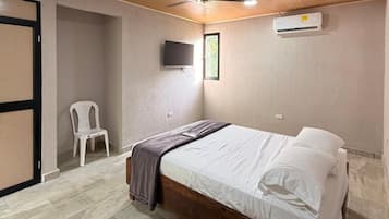 Un dormitorio con cama, ventilador de techo, televisor montado en la pared y aire acondicionado.