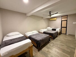 A hotel room with four single beds, a ceiling fan, an air conditioning unit, and a wooden floor.