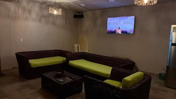 A living room with a sofa, a coffee table, and a television displaying 'BLACK COFFEE' on the wall.
