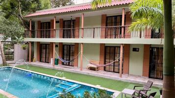 Un edificio de dos pisos con piscina, asientos exteriores y una hamaca.