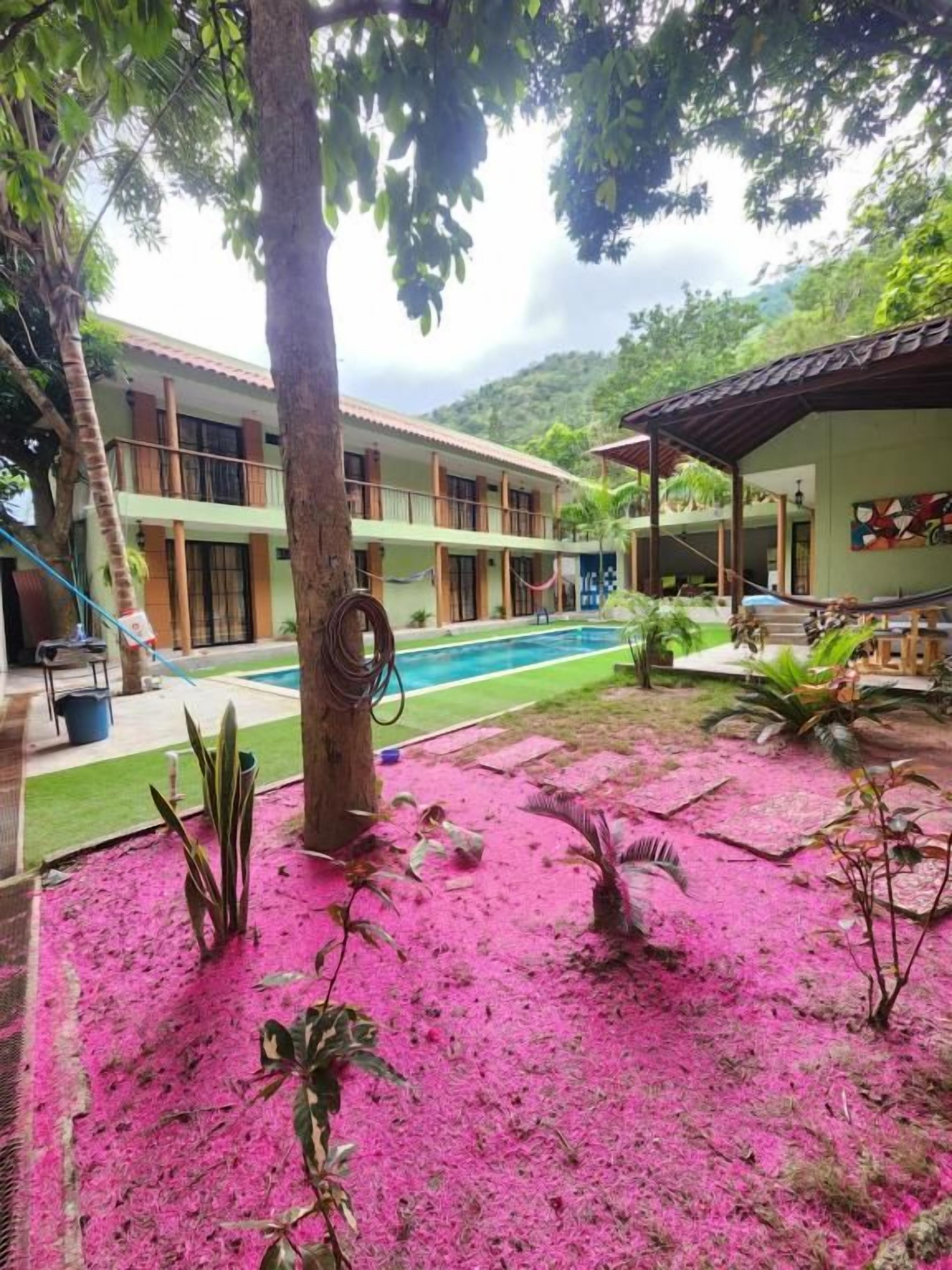 Un hotel con piscina, un patio cubierto y un jardín con arena rosa.