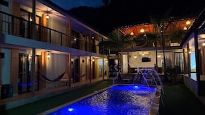 A hotel with a swimming pool, outdoor seating, and a covered area with lights.