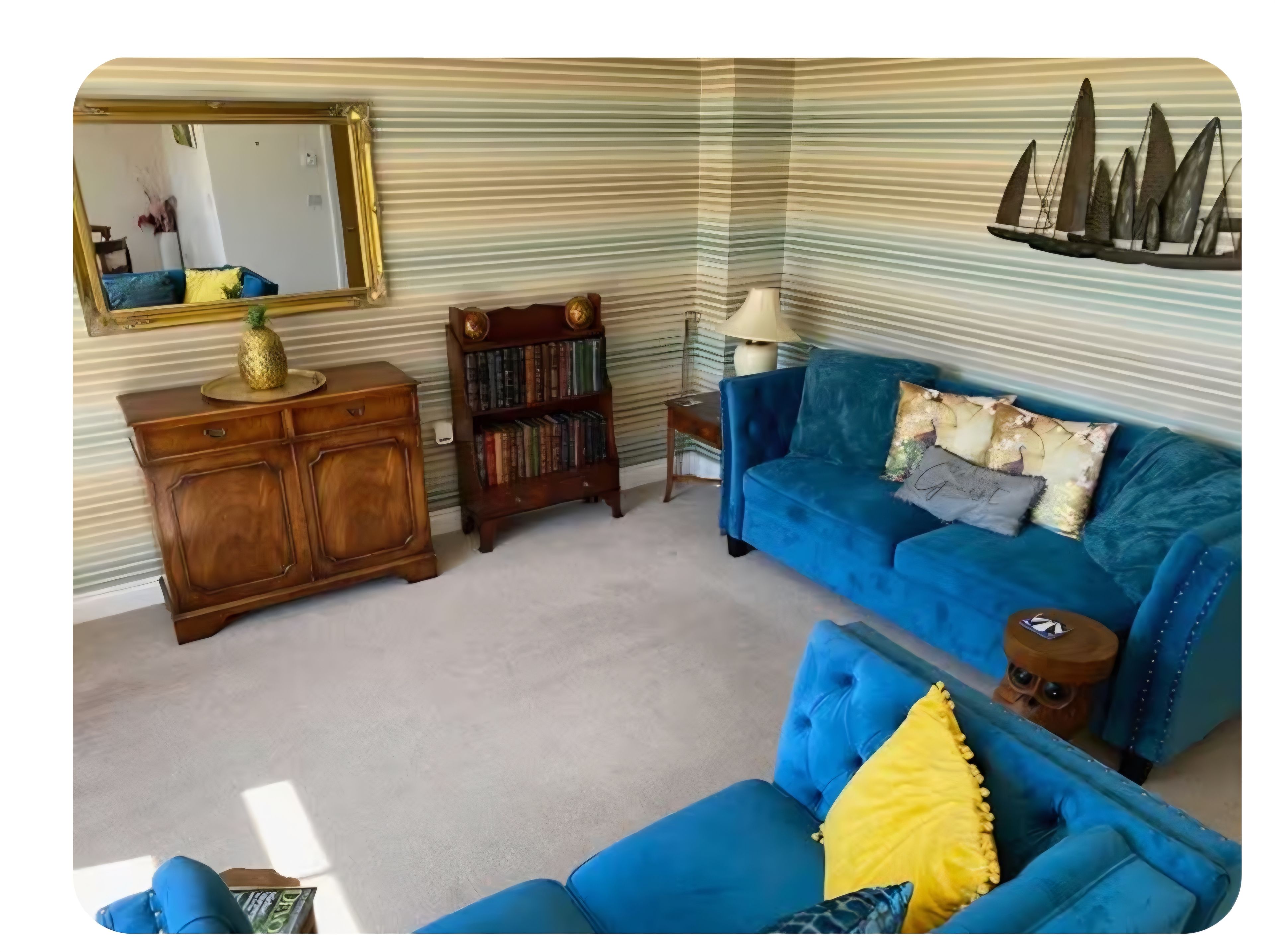 A room with a blue sofa, a wooden cabinet, a bookshelf, and a mirror.