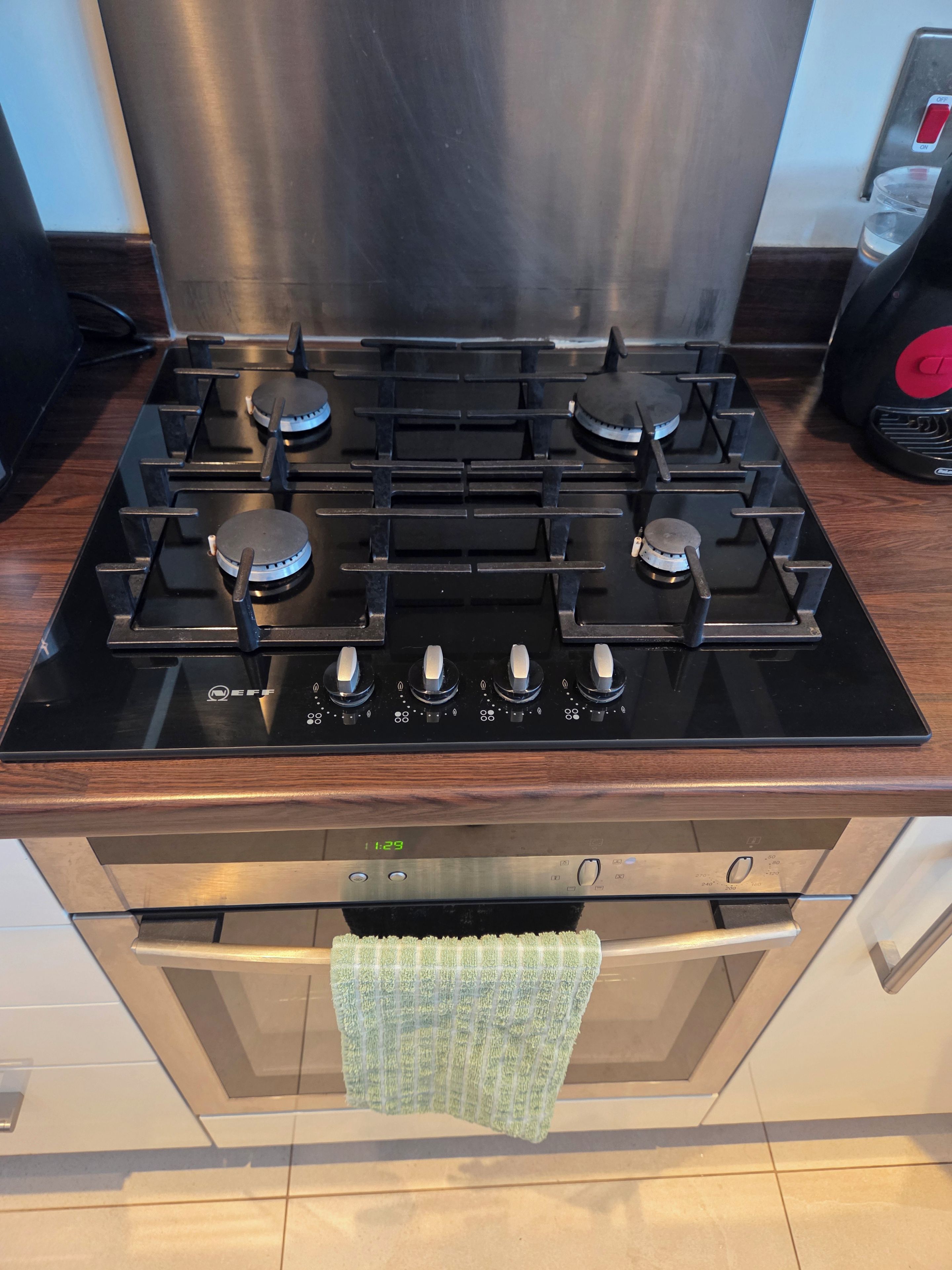 A kitchen with a black stove, stainless steel range hood, and a green towel hanging over the oven.