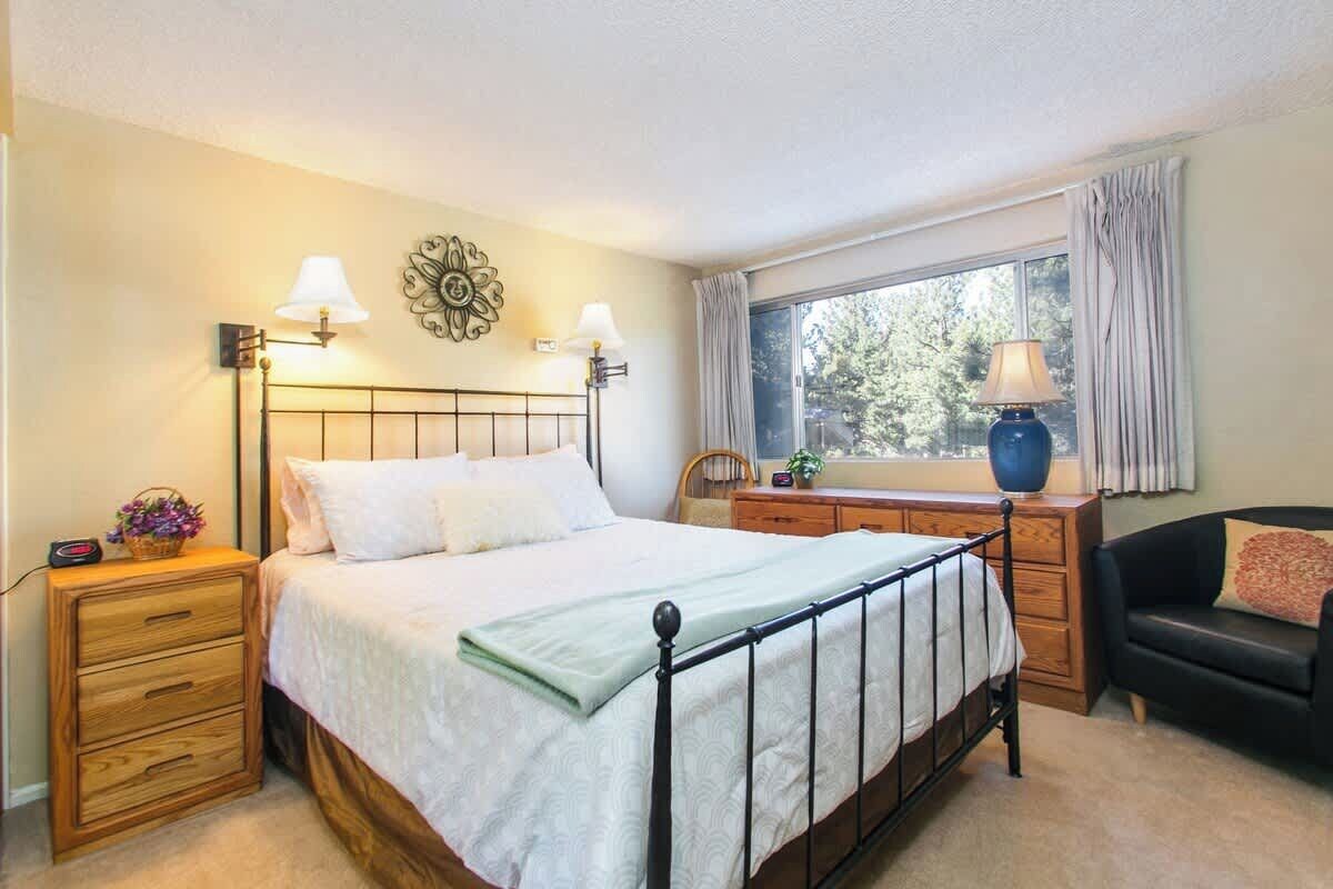 A bedroom with a bed, bedside tables, a dresser, a window with curtains, and a chair.