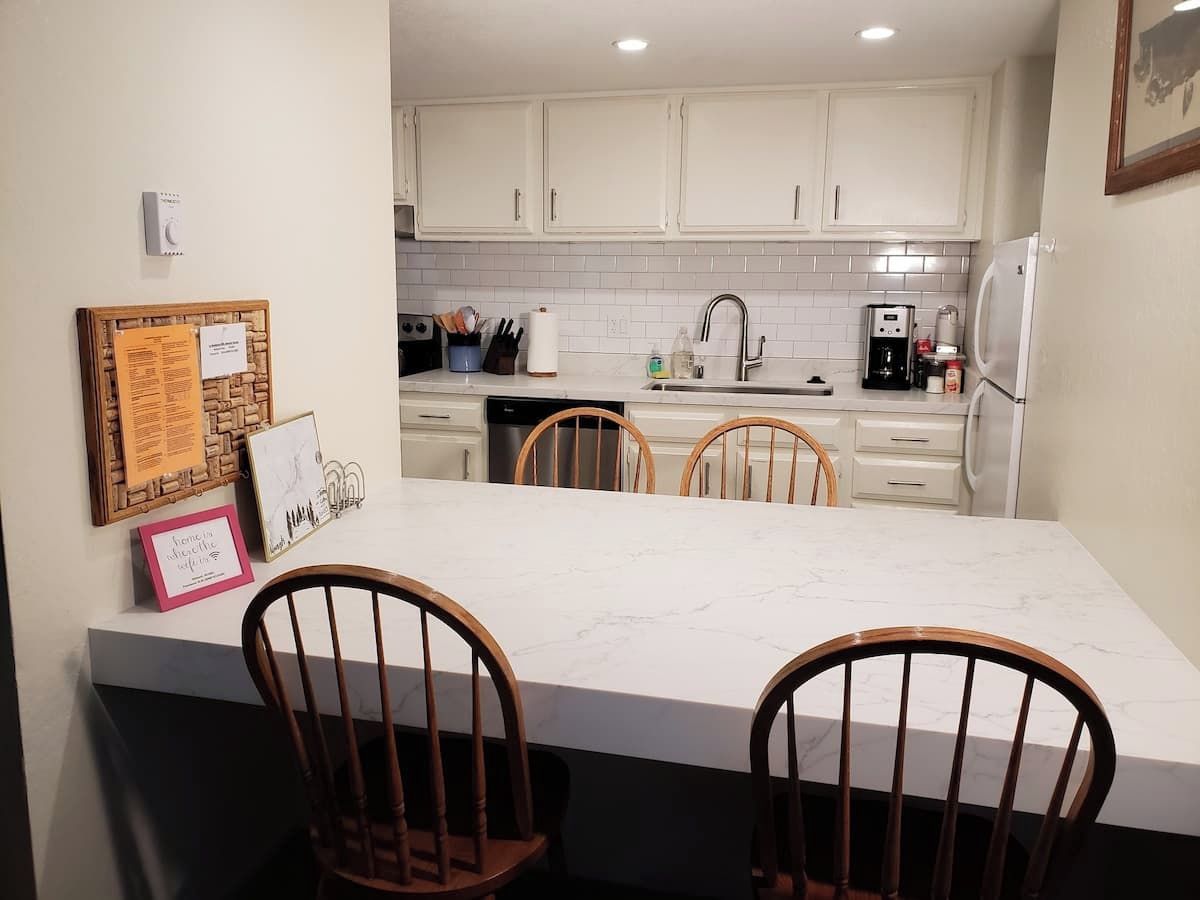 A kitchen with white cabinets, a marble countertop, and wooden chairs.