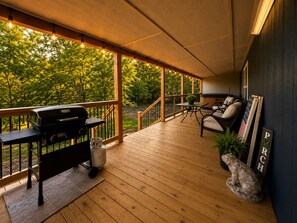 Una terrassa coberta a l'aire lliure amb una barbacoa, zona de seients i vista als arbres.