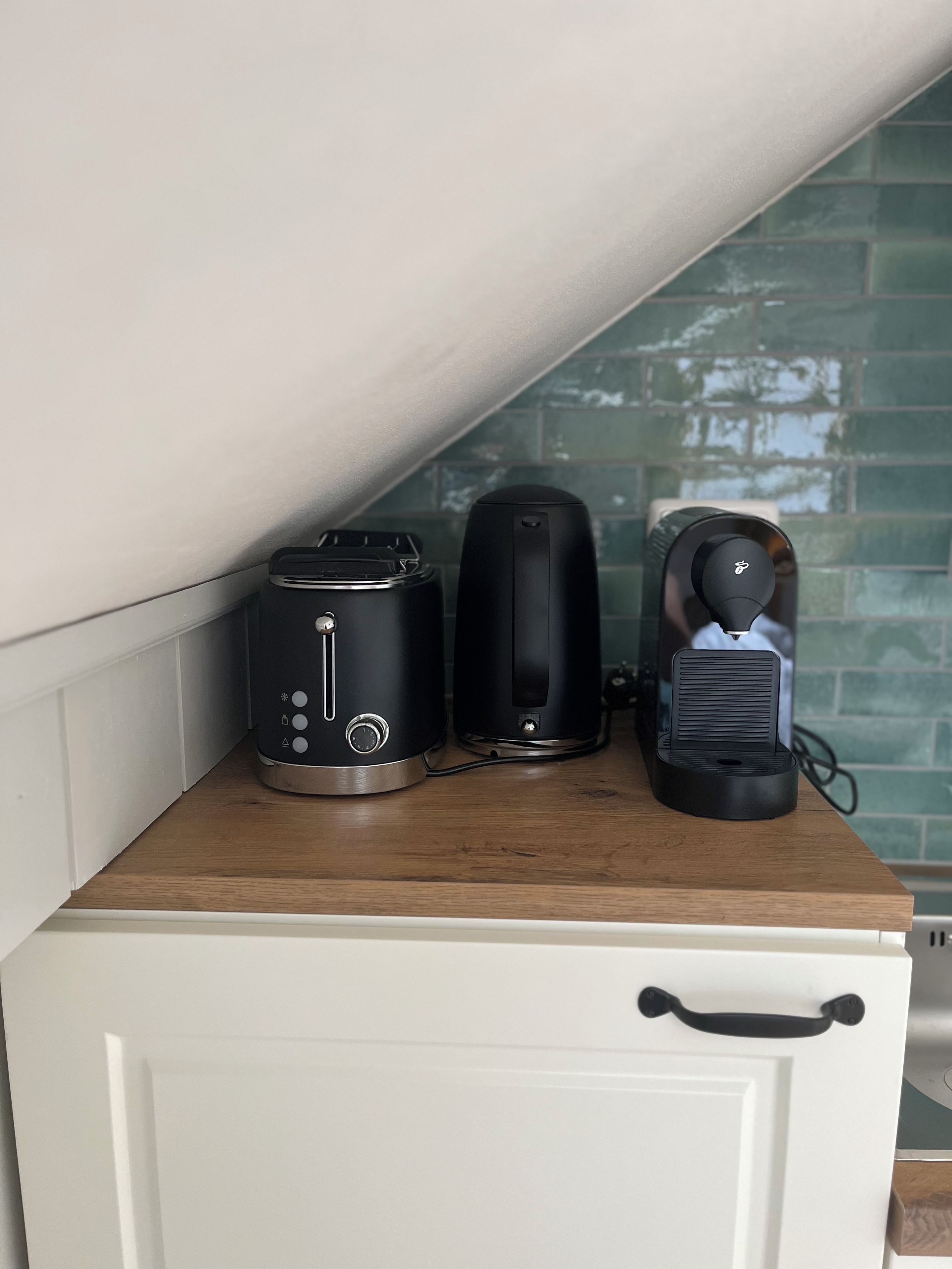Eine Küchenzeile mit einem Toaster, einem Wasserkocher und einer Kaffeemaschine auf einer Holzausziehtafel.