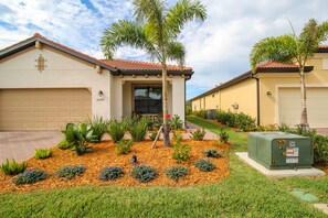 A residential property with a garage, a well-maintained garden with various plants, and a utility box. - Sarasota National Golf Villa - 2BR+Den, 2 Golf Memberships, Clubhouse Amenities (Venice)