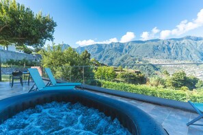 A hot tub with a mountain view, outdoor seating, and a stone wall. - Star Lodge by Atlantic Holiday (São Vicente)