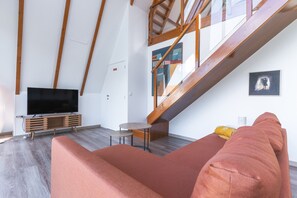 A modern living room with a TV, wooden beams, a staircase, and artwork on the walls. - Star Lodge by Atlantic Holiday (São Vicente)