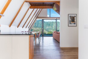 A modern interior with a dining area, a sofa, and a large window offering a mountain view. - Star Lodge by Atlantic Holiday (São Vicente)