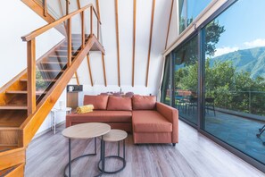 A modern interior with a wooden staircase, a sectional sofa, and a large window offering a mountain view. - Star Lodge by Atlantic Holiday (São Vicente)