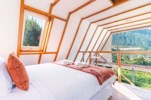 Ein Schlafzimmer mit einem Bett, einem Fenster und Blick auf eine Berglandschaft.