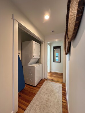 A laundry room with a washing machine and dryer, a wooden floor, and a hallway leading to a door with a mirror. - Historic Two Bedroom Apartment Overlooking Olde Towne Daphne (Daphne)