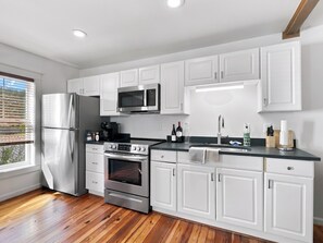 A modern kitchen with stainless steel appliances, white cabinetry, and a wooden floor. - Historic Two Bedroom Apartment Overlooking Olde Towne Daphne (Daphne)