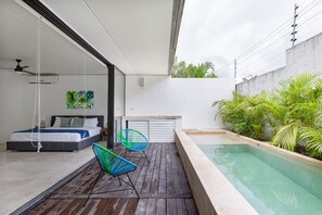 Un dormitorio moderno con cama, un pequeño rincón de descanso con sillas y vistas a una piscina.
