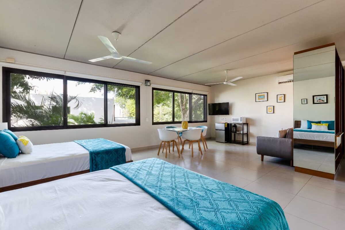 A hotel room with two beds, a dining area, a kitchenette, and a TV.