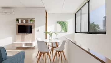 Una sala de estar moderna con un televisor de pantalla plana, un comedor con una mesa y sillas blancas, y un ventanal con vistas.