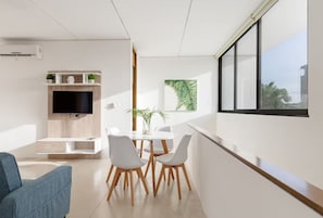 A modern living room with a flat-screen TV, a dining area with a white table and chairs, and a large window with a view. - Residencial Palmaris by Homirent (Cancún)