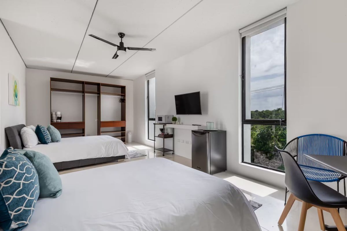 A modern hotel room with two beds, a desk, a TV, and a large window.