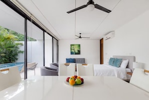 A modern hotel room with a balcony, a dining area with a fruit bowl, a bed with white bedding, and a ceiling fan. - Residencial Palmaris by Homirent (Cancún)